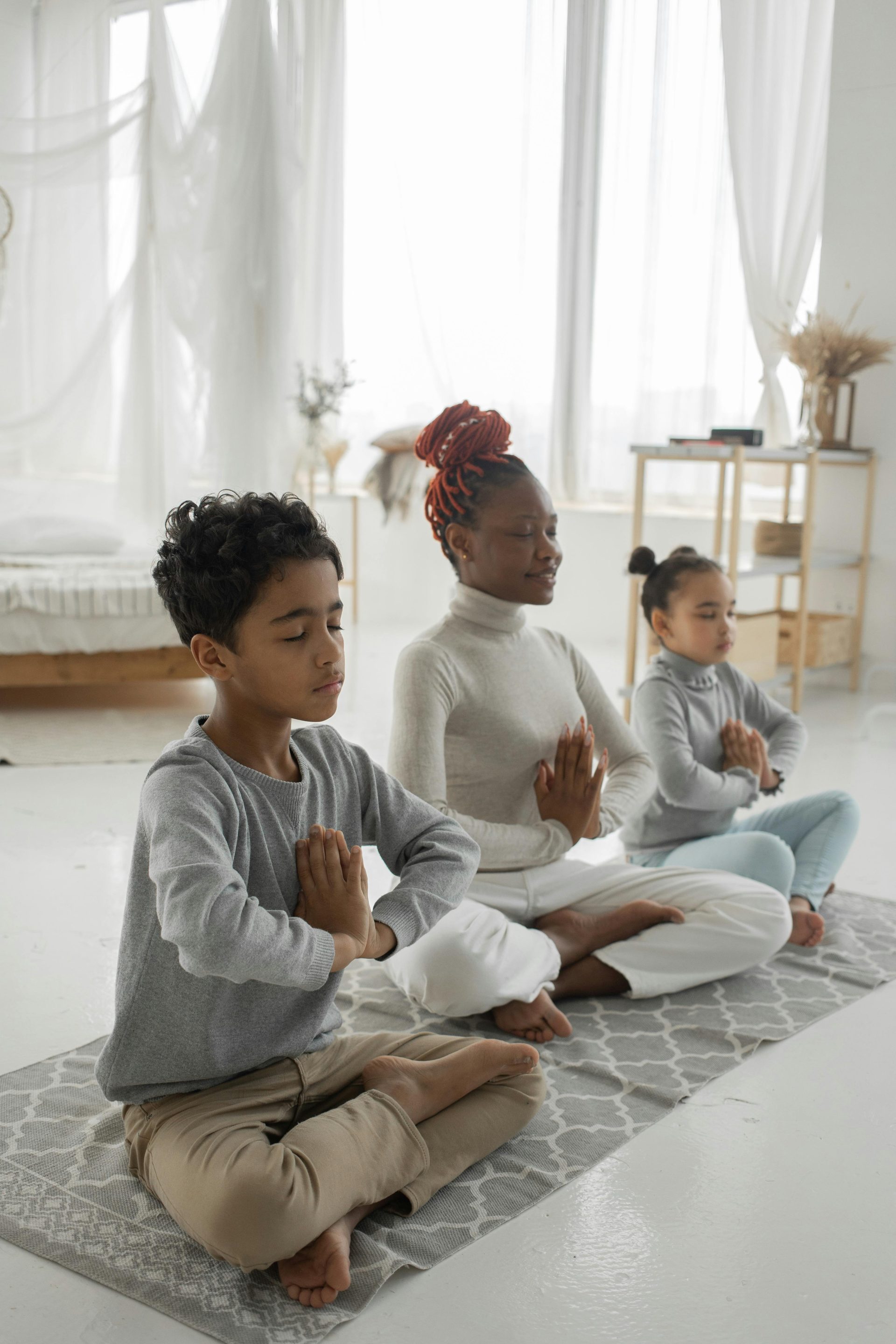Cute ethnic children with young mom meditating together with closed eyes at home